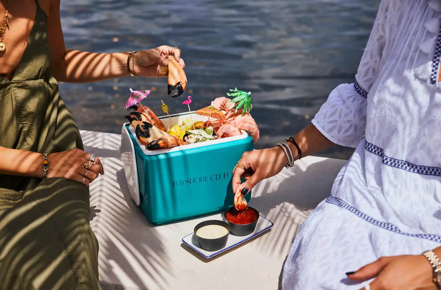 A cooler full of seafood with people dipping the seafood in sauces by the water at Bayshore Club, found on OpenTable.
