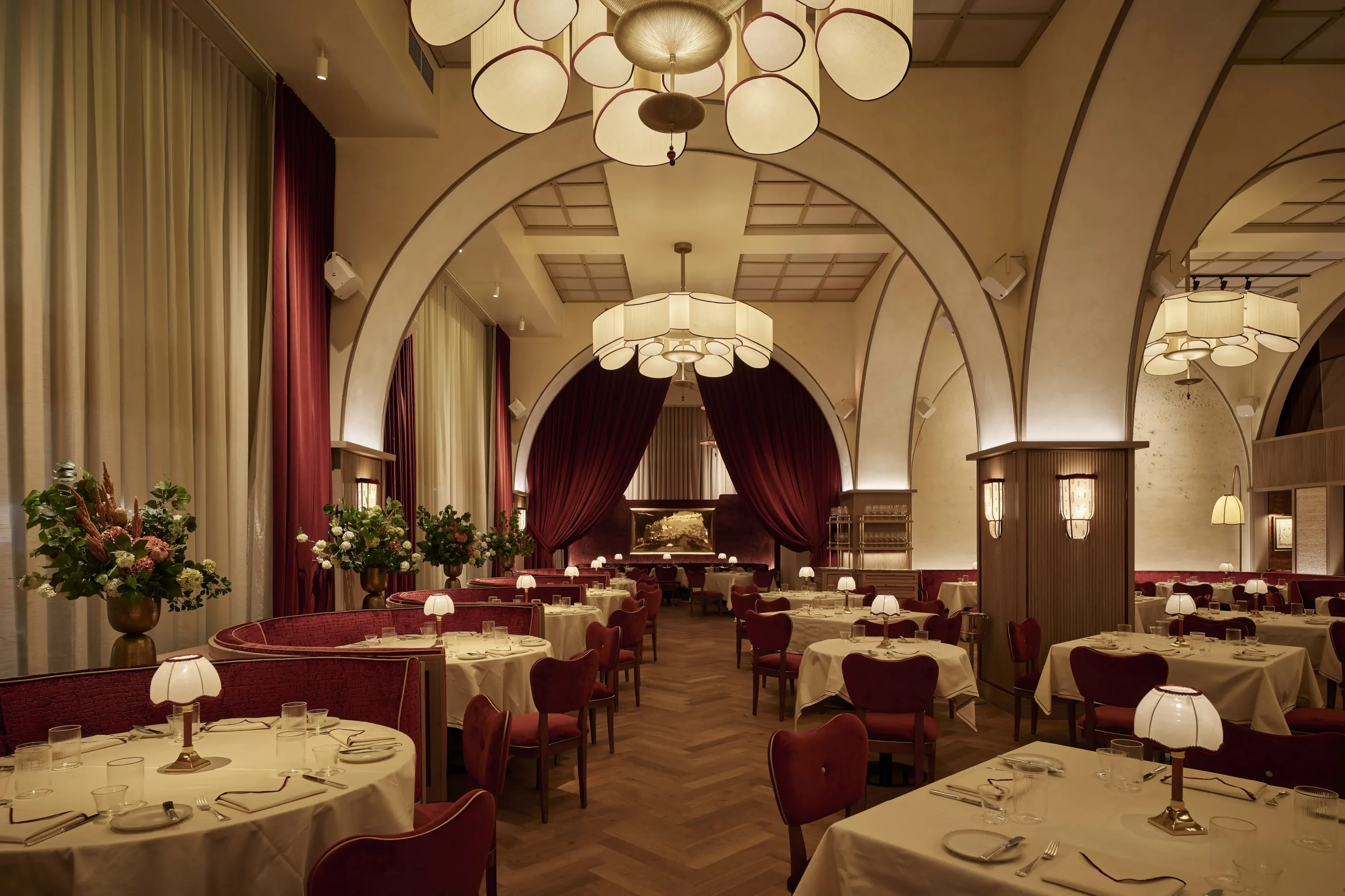The interior of NYC restaurant Crane Club featuring dark red booths and arches in the dining room