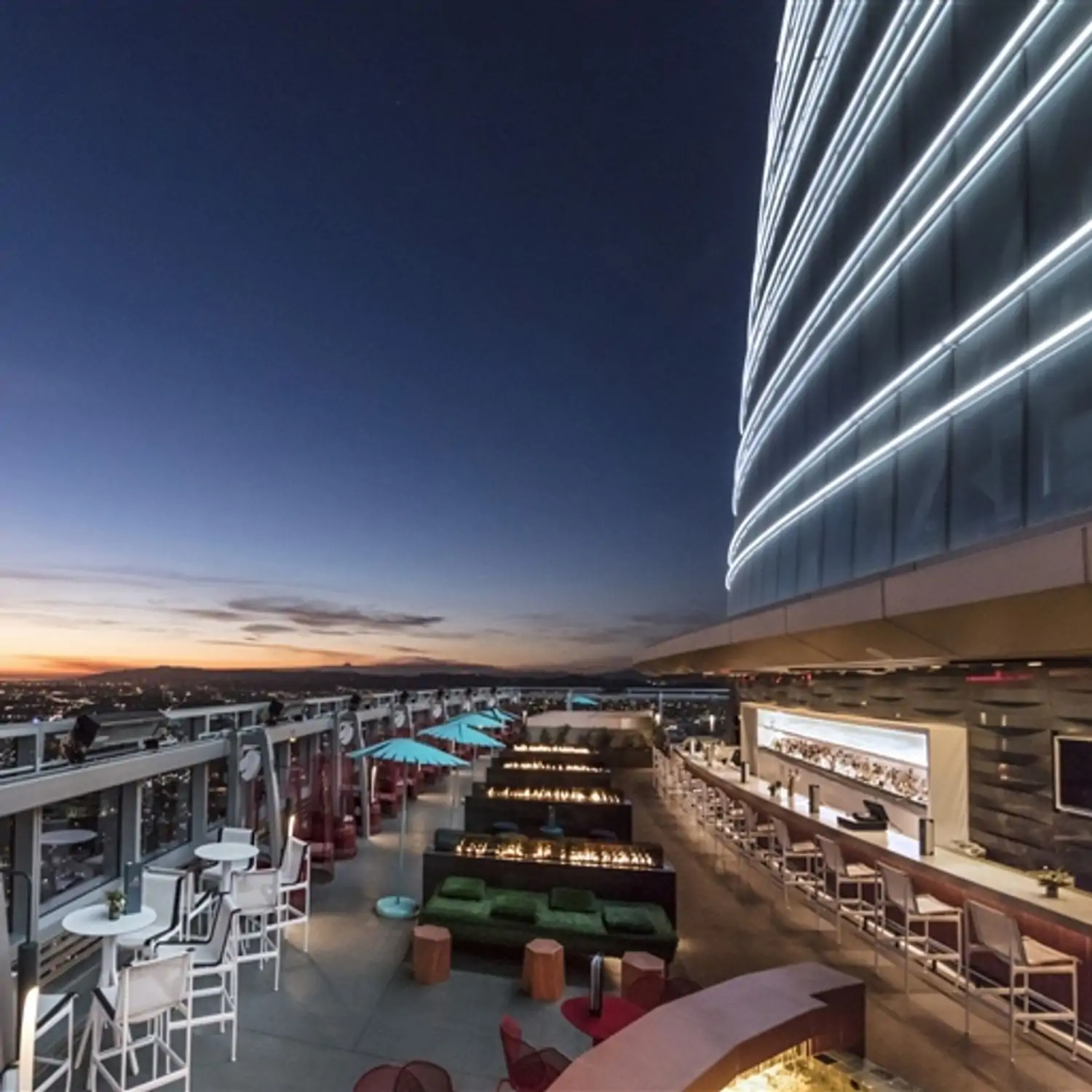 A rooftop terrace with lounge chairs, a long bar, and fire pits at Spire73, in Los Angeles. Book on OpenTable.