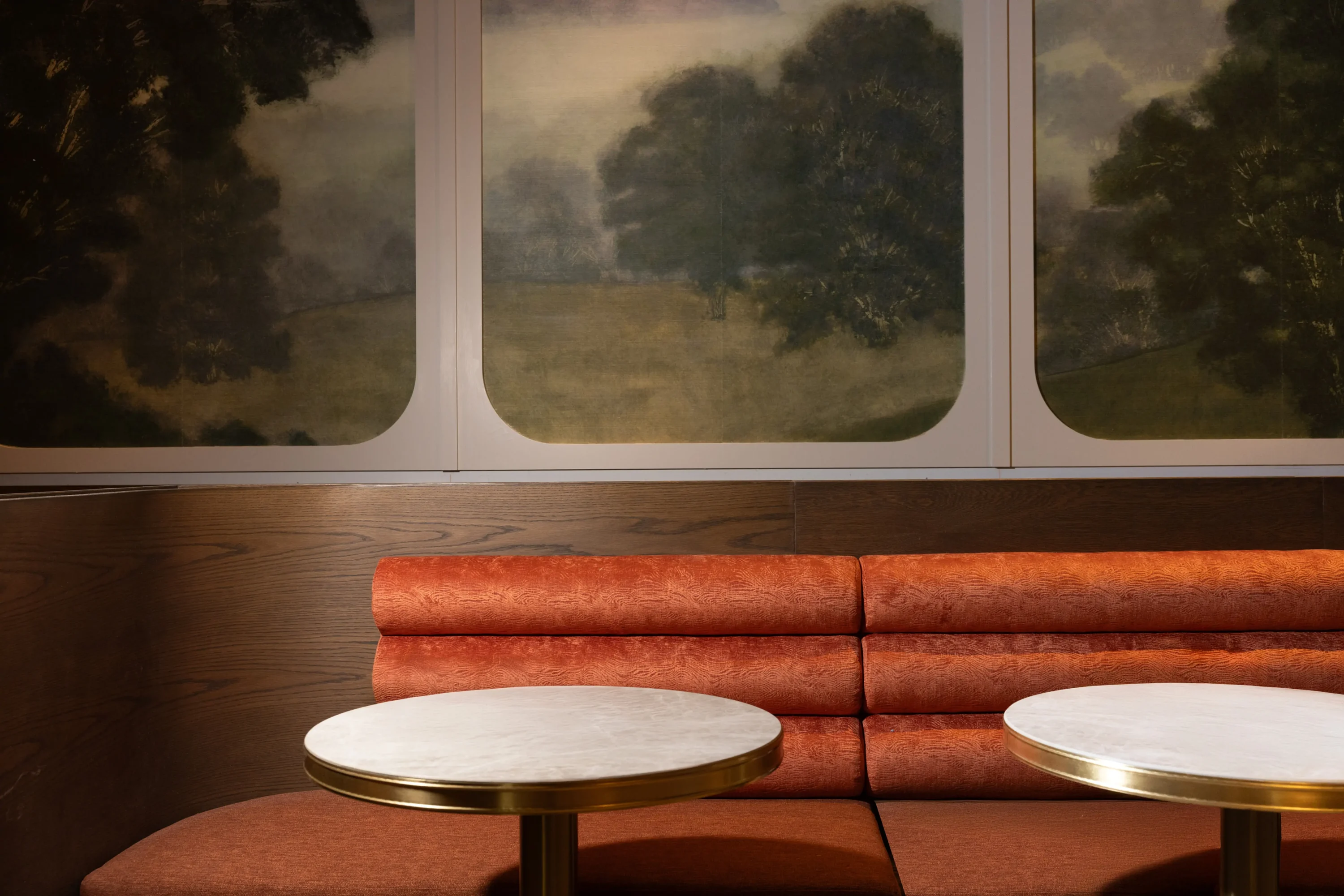 A plush burnt orange banquettes framed by a mural of the English countryside at Haymarket in NYC. Book on OpenTable.