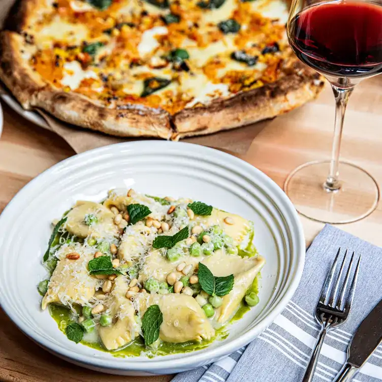 Ravioli and pizza dish on a table with wine at Indaco