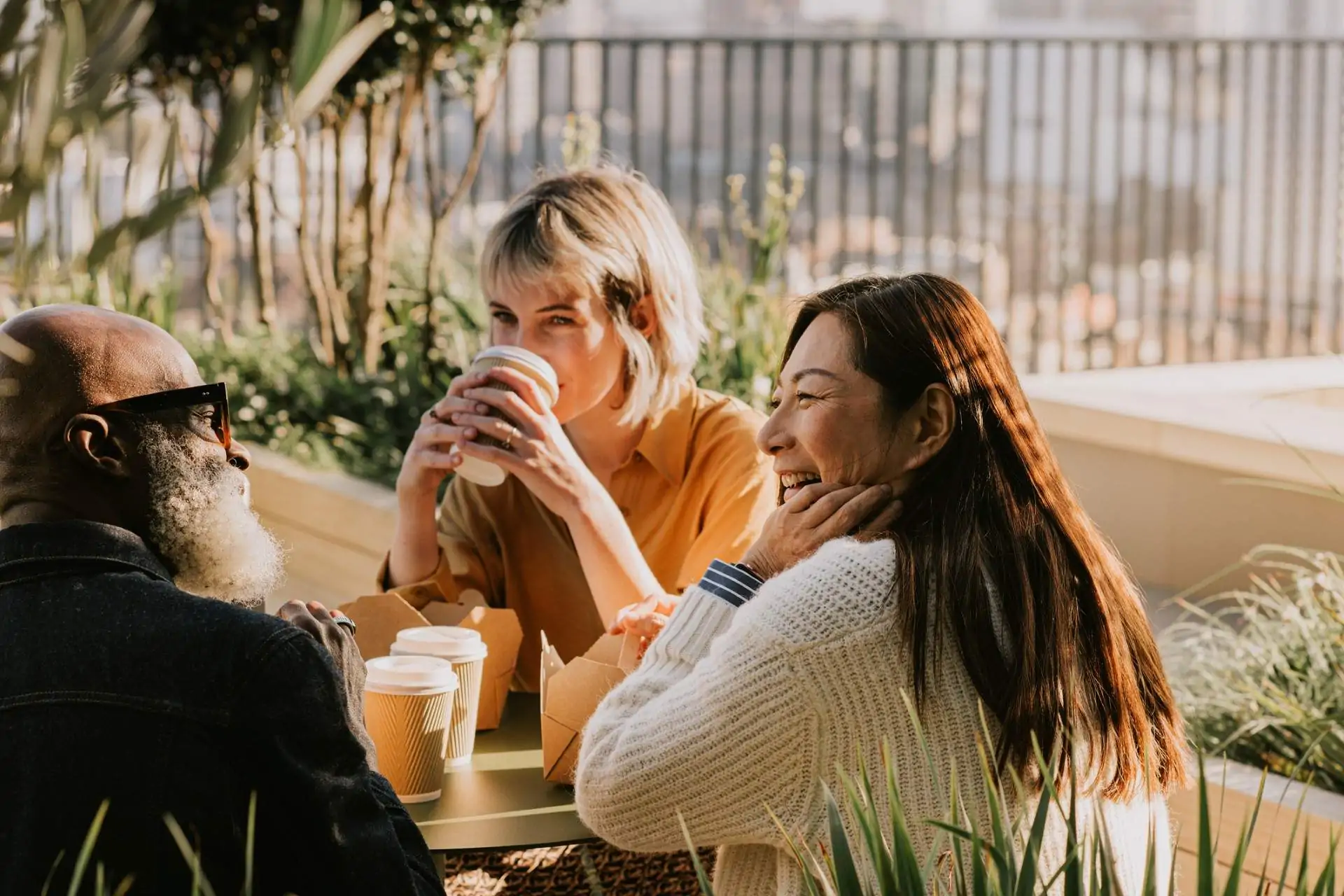 Image depicts two people sitting at a restaurant drinking orange drinks. One is laughing with their hand on their head.
