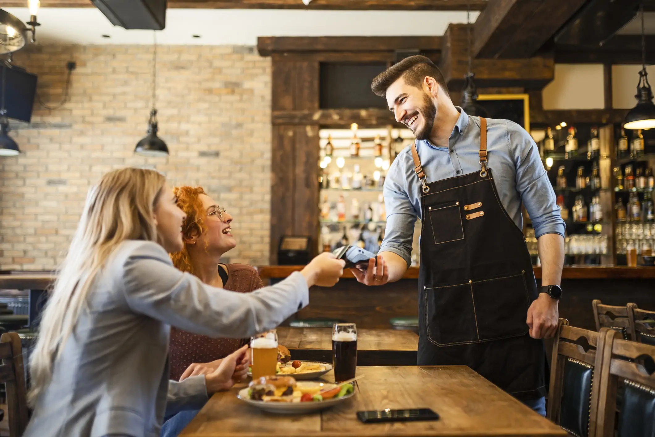 male server is showing the woman diner the card reader to pay for her meal with her friend.
