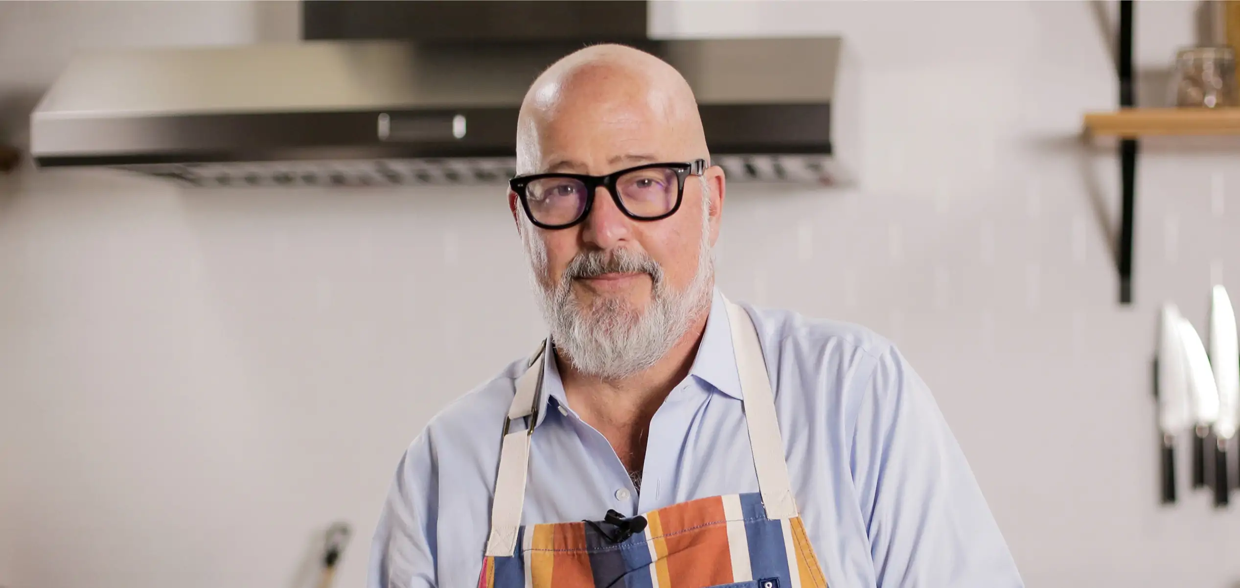 A portrait of author and chef Andrew Zimmern wearing an apron in a professional kitchen setting.